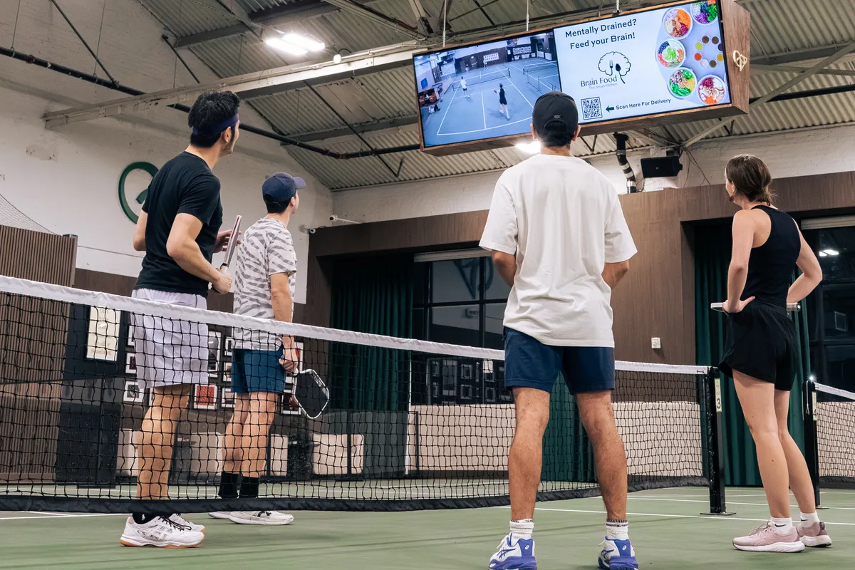 Four players standing at the net on an indoor court at Velto during open play